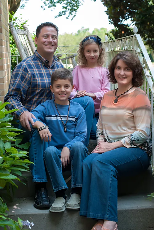Dr. Ben Savoie pictured with his family. His wife, daughter, and son sit next to him on the steps to their home